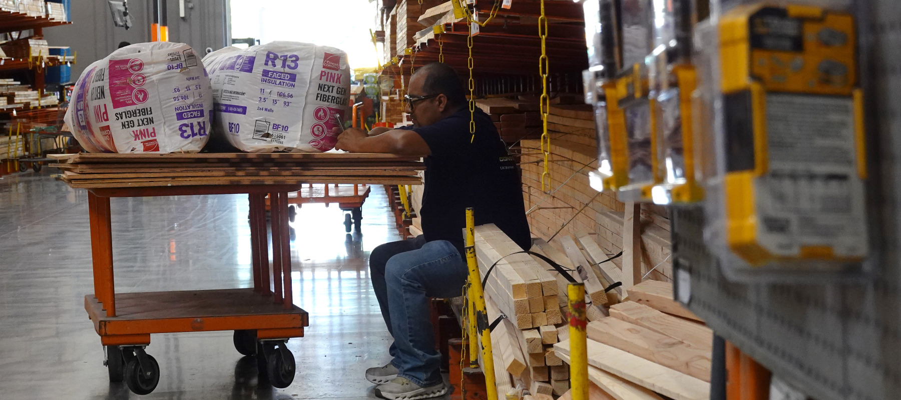 A customer looks at his phone as he sits with his cart at a Home Depot store.