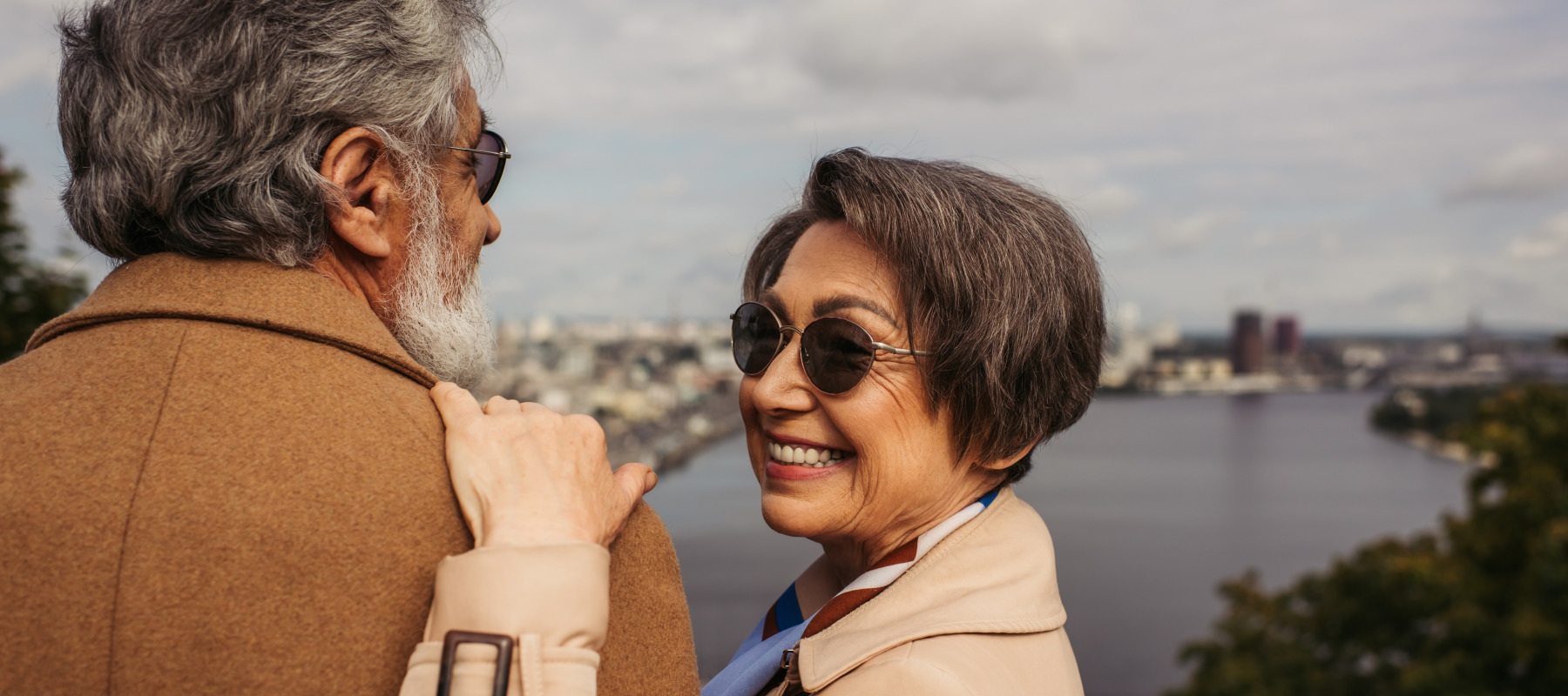 Man and woman looking out over mountain scene, man's back to the camera and woman looking back, smiling.