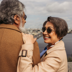 Man and woman looking out over mountain scene, man's back to the camera and woman looking back, smiling.