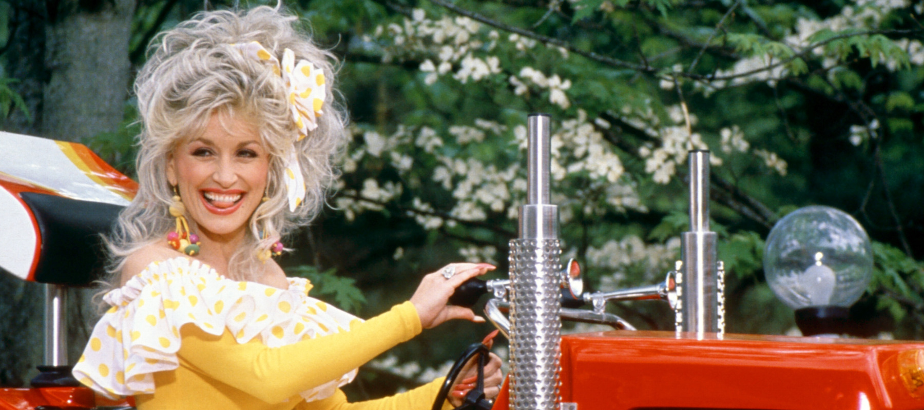 Dolly Parton smiles, posing on a truck at Dollywood in 1997.