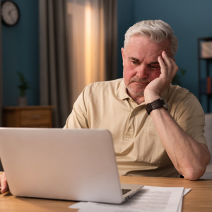An older American man is frustrated as he looks at his computer.