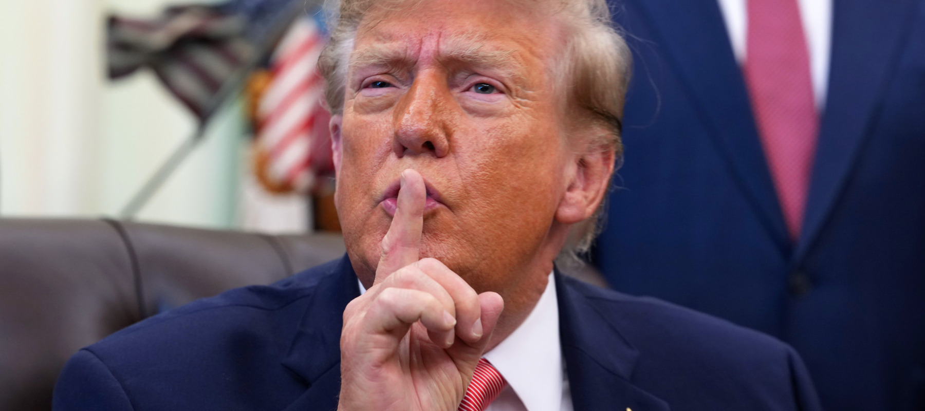 Trump gestures to reporters to be quiet during an event in the Oval Office.