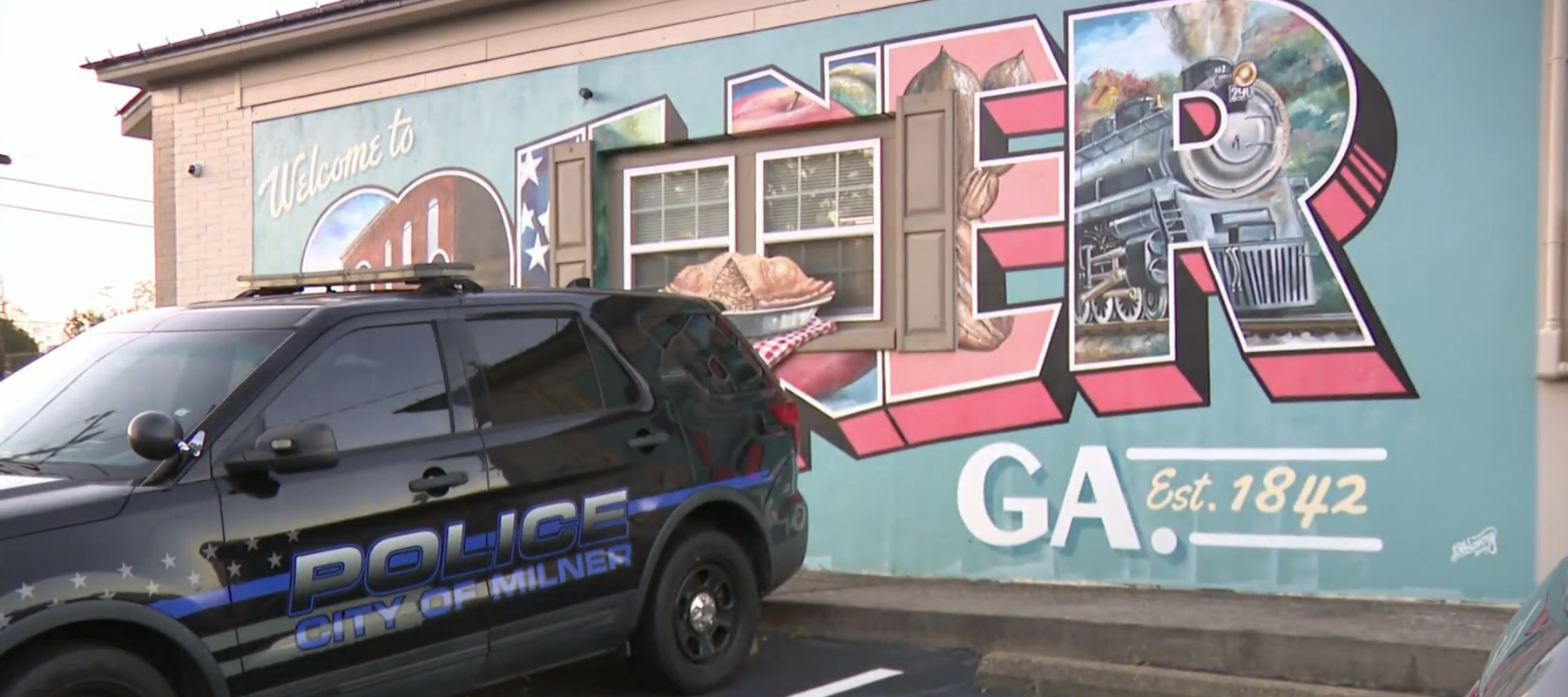 A Milner Police Department truck is parked in front of a City of Milner mural.