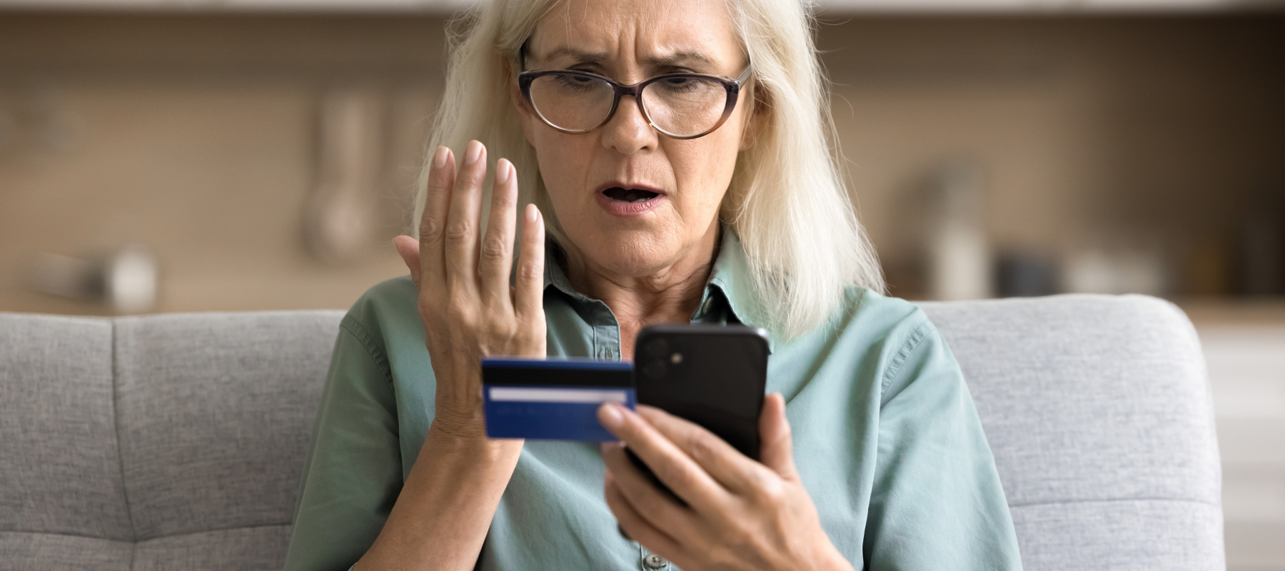 An woman looks at her smartphone, as well as her credit card, with concern.