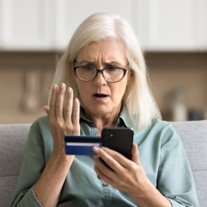 An woman looks at her smartphone, as well as her credit card, with concern.
