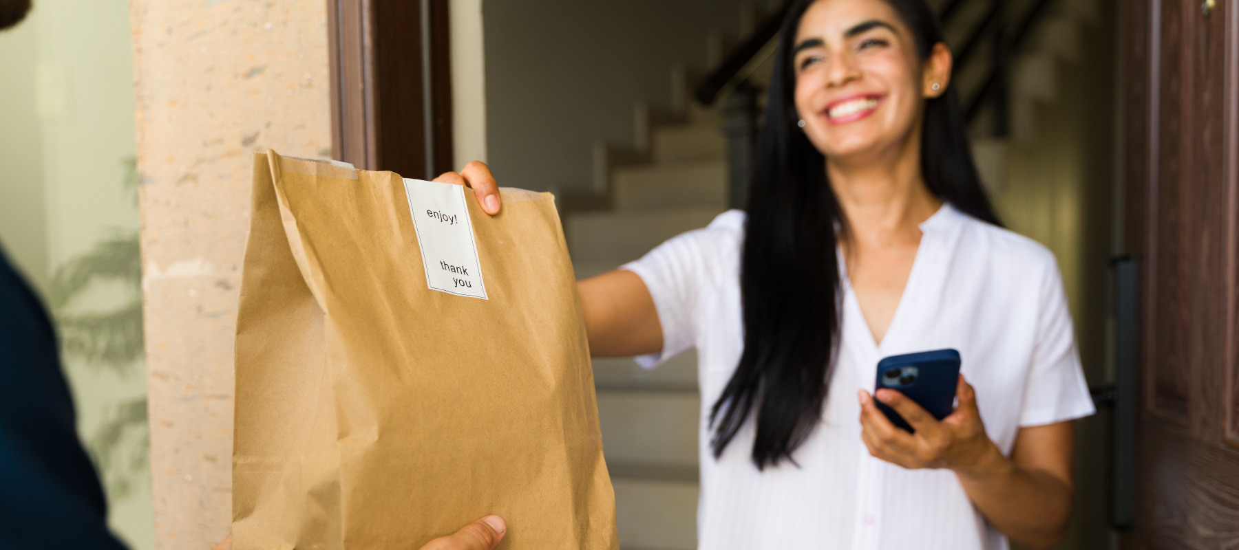 A smilling woman accepts her food delivery order at her home's front door