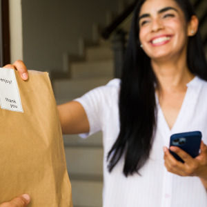 A smilling woman accepts her food delivery order at her home's front door