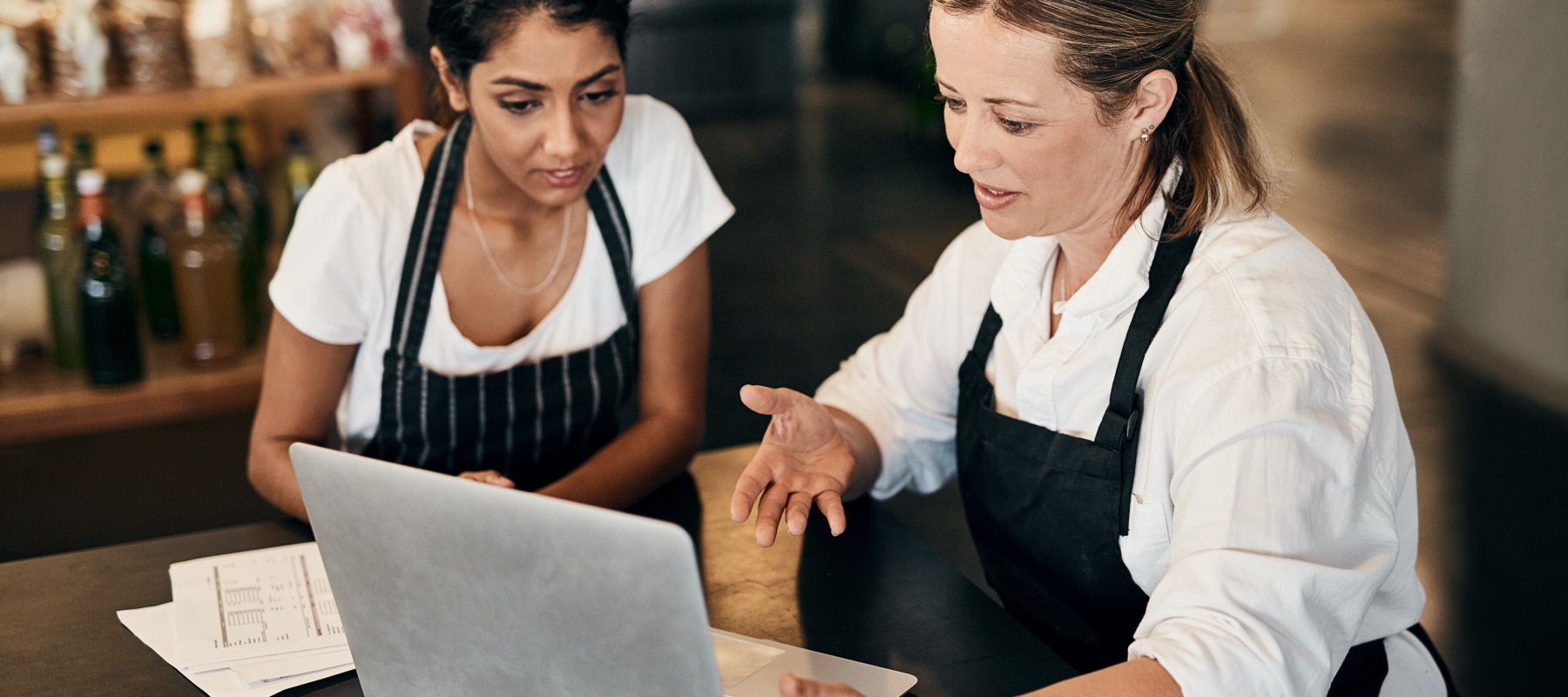 Two female restaurant workers looking at a laptop screen.