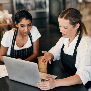 Two female restaurant workers looking at a laptop screen.