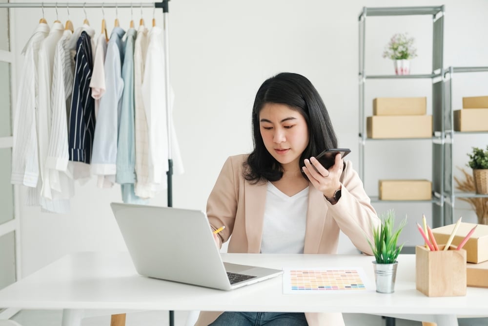 a young businesswoman on the phone, sitting in front of a laptop, in her store