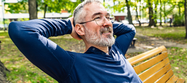 Man in his late 40s sitting on a bench in an urban park.