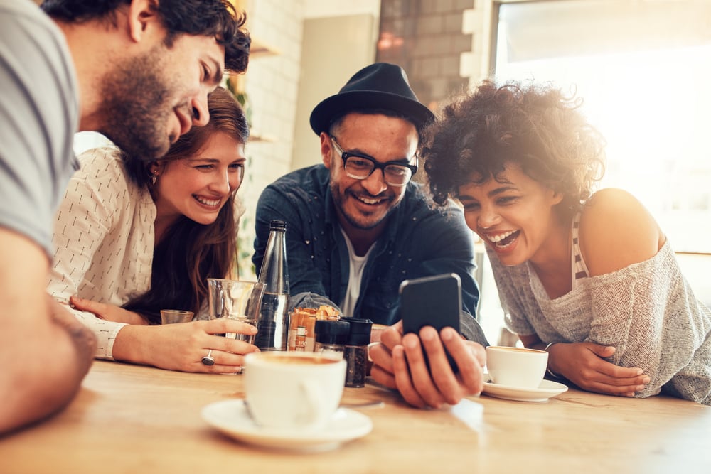 a group of friends looking at a phone at the coffee shop