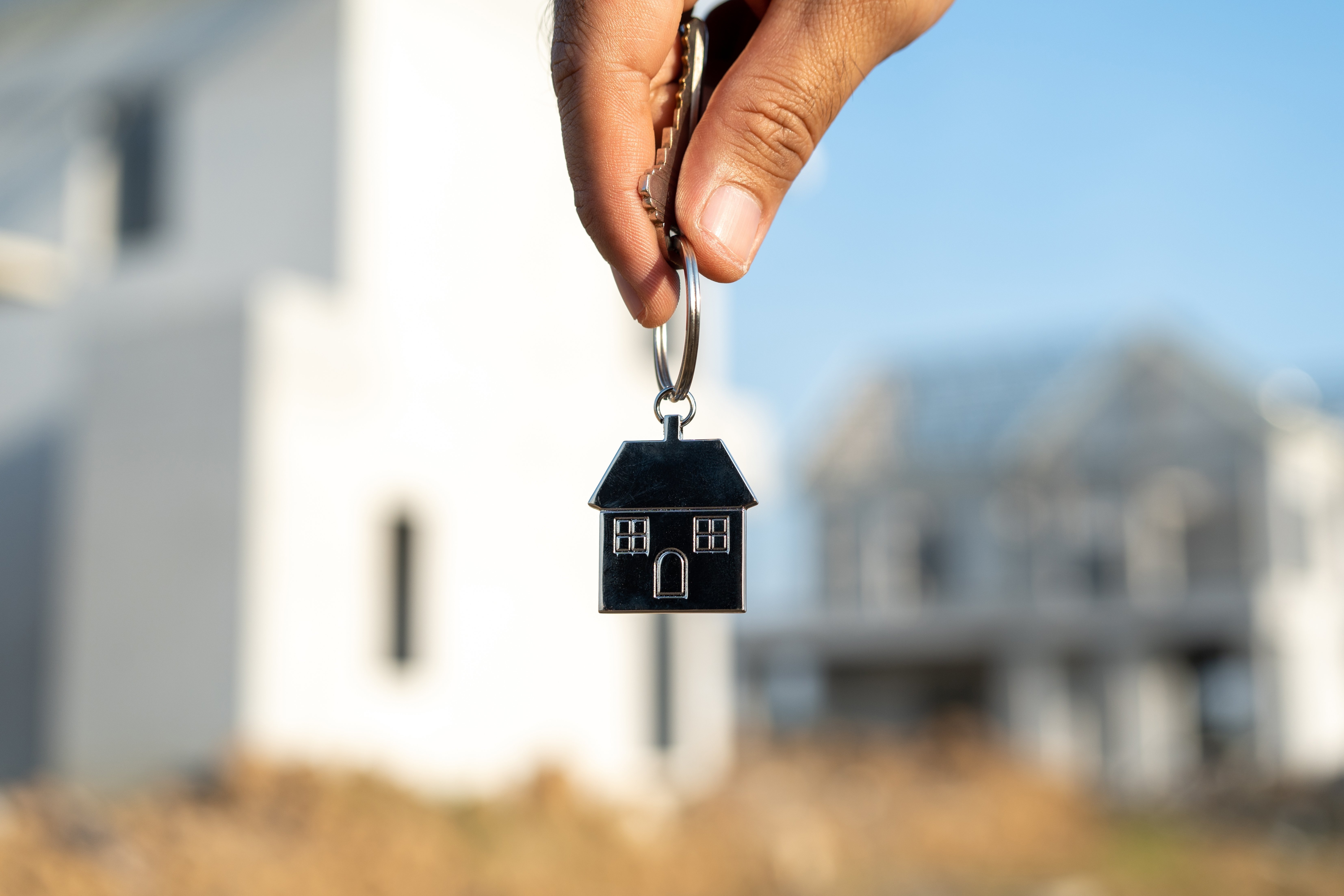 Close up male hand holding house key with sunlight. Real estate agent at construction site. New home purchase sales or rent. Choose Planning to buy property