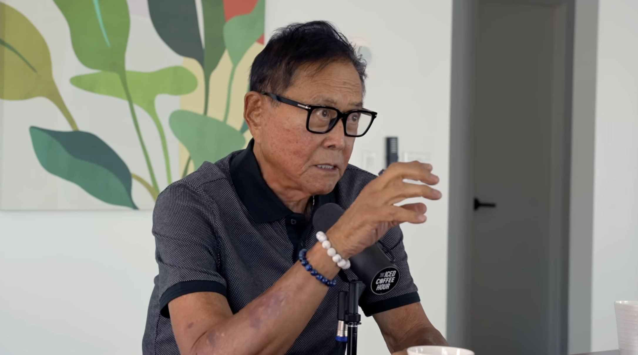 Robert Kiyosaki gestures broadly while speaking into a microphone.